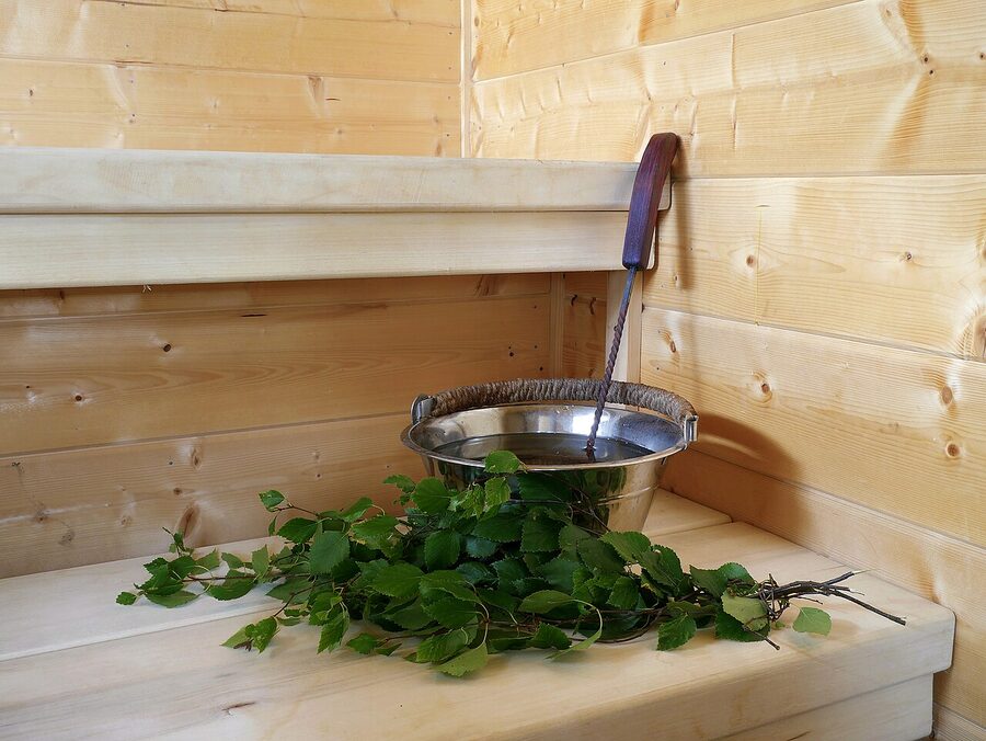 A wooden water bucket with a ladle and a fresh birch vihta on a sauna bench