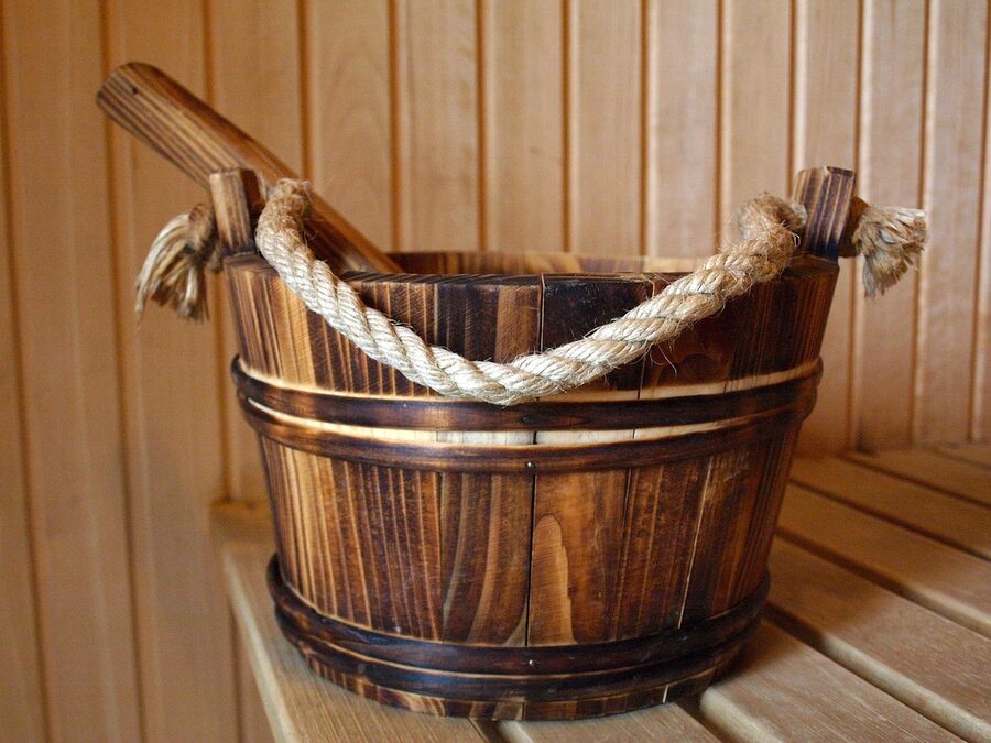 A wooden water bucket and ladle on a sauna bench