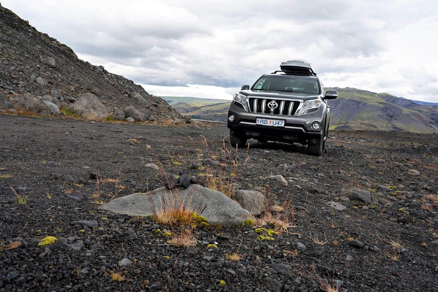 A small car parked in front of an Icelandic mountain landscape
