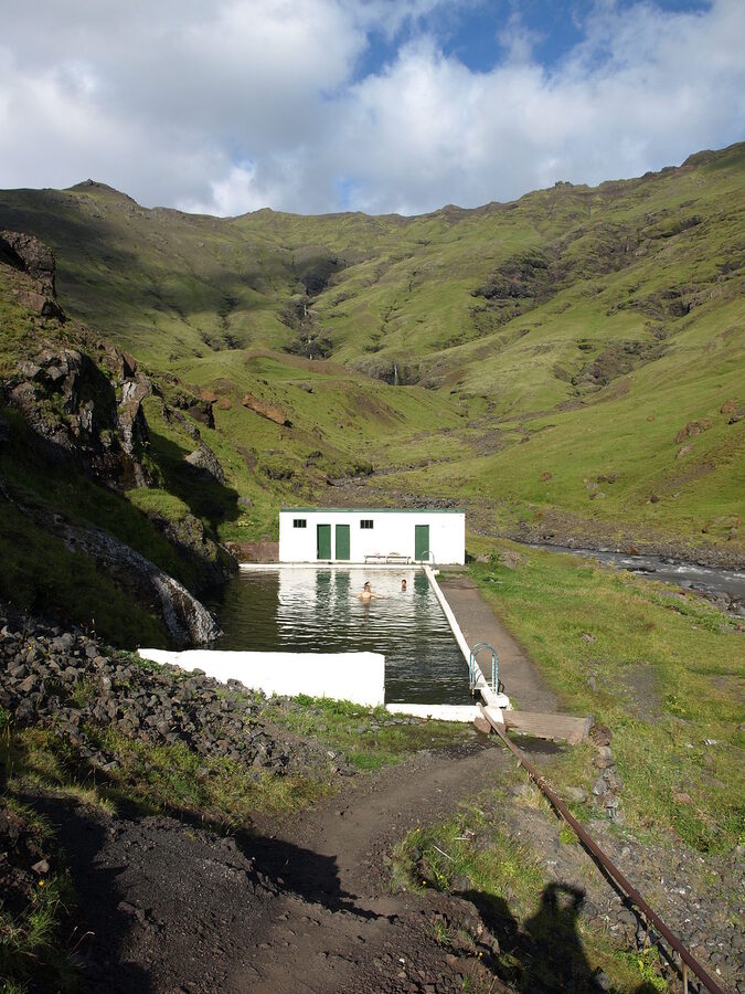 The Seljavallalaug pool seen from the slope, a turquoise rectangle between two valley walls