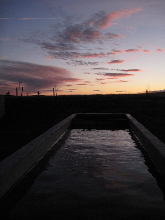 A small Icelandic hot pot at sunset with steam against the orange sky