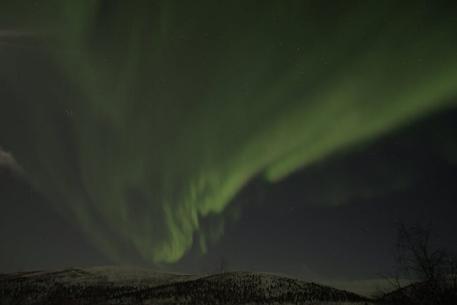 Green aurora borealis over a snow-covered ridge under starlight