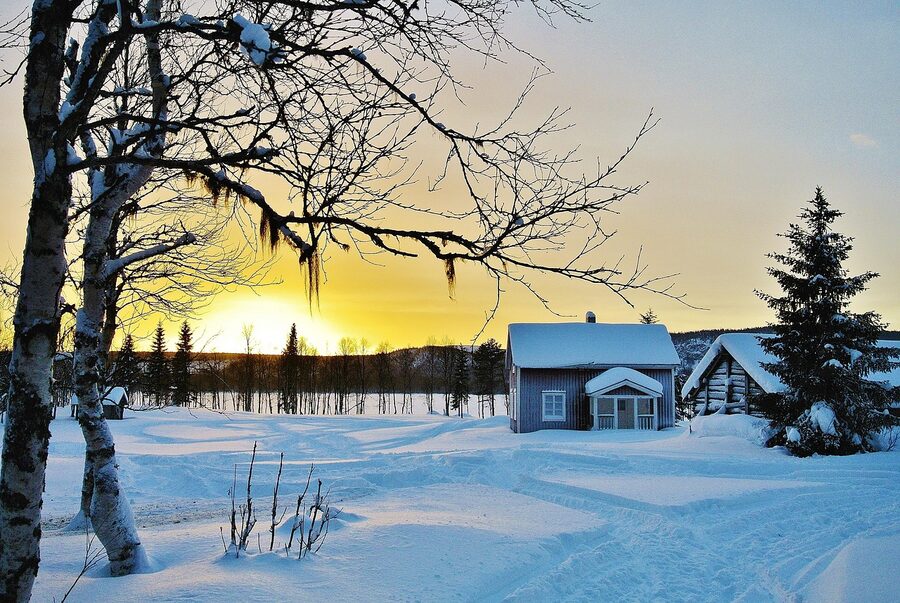 A red wooden cottage in a Norrland snowfield at sunset