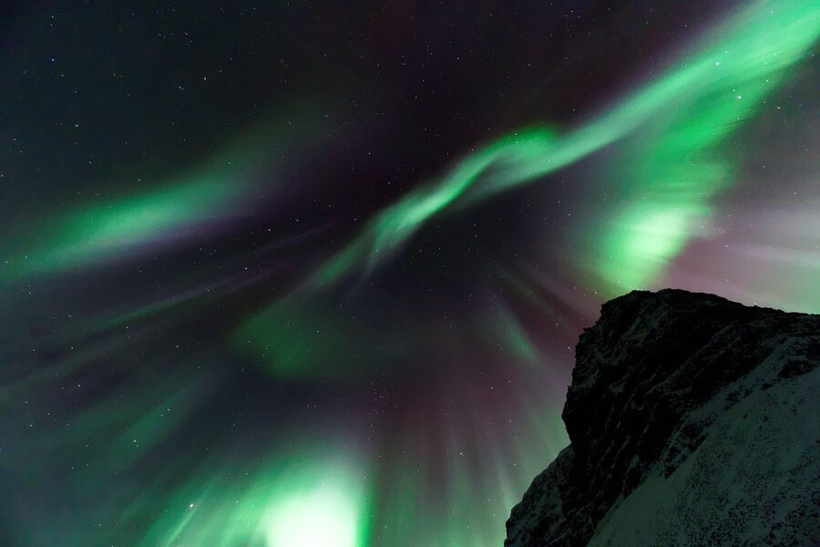 Aurora borealis sweeping over a dark mountain landscape