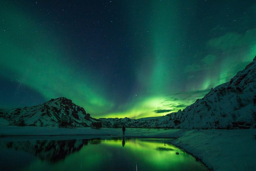 Silhouette of an aurora photographer with camera and tripod against the night sky