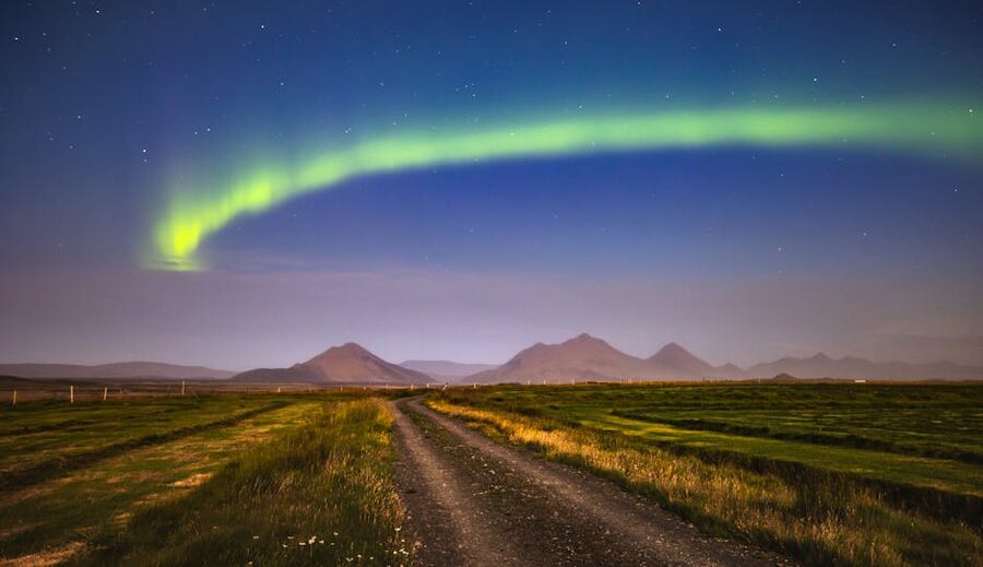 Aurora borealis over a rural Icelandic landscape with a dirt road