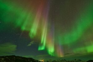 Vivid aurora borealis dancing over Icelandic landscape, captivating night spectacle.