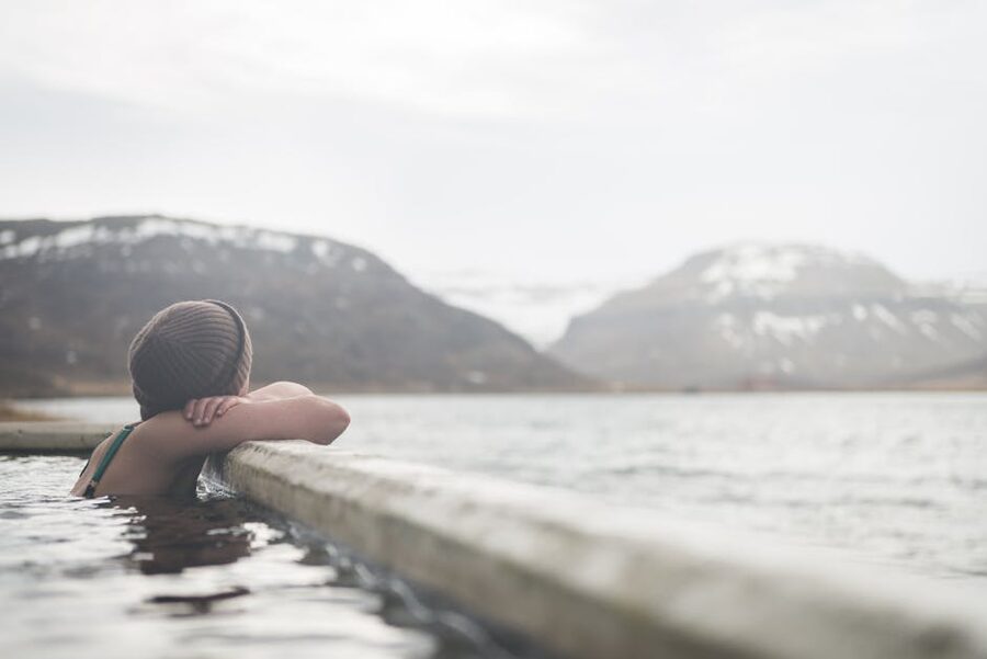 A traveller in a knit hat soaking in a geothermal pool, seen from behind
