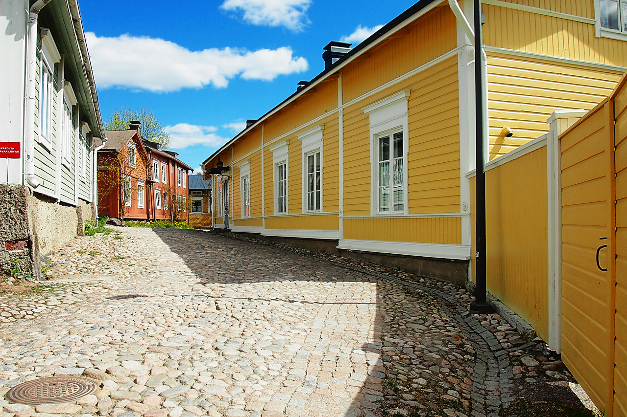 A narrow alleyway in Porvoo Old Town between two timber houses, leading down toward the river