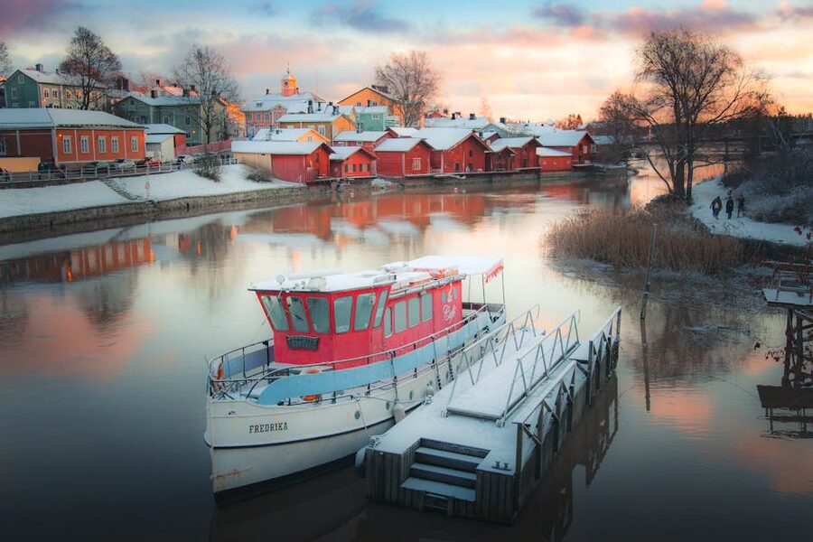 Snow-covered boats reflecting in Porvoo's historic harbor during a winter sunset