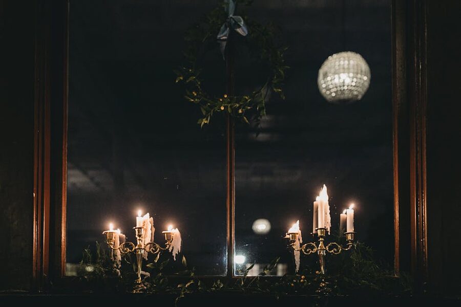 Glowing candles in a window with snow falling outside, framed against a dark winter evening