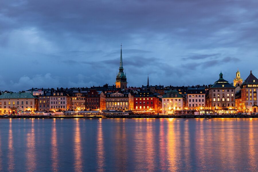 Gamla Stan in winter with old Stockholm buildings, snow on the cobbles, and a single figure walking under streetlights