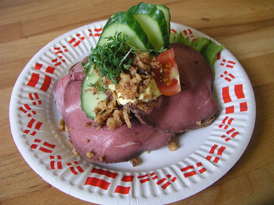 A precisely-plated open-faced sandwich on rugbrød with herring and trimmings at a Copenhagen smørrebrød restaurant