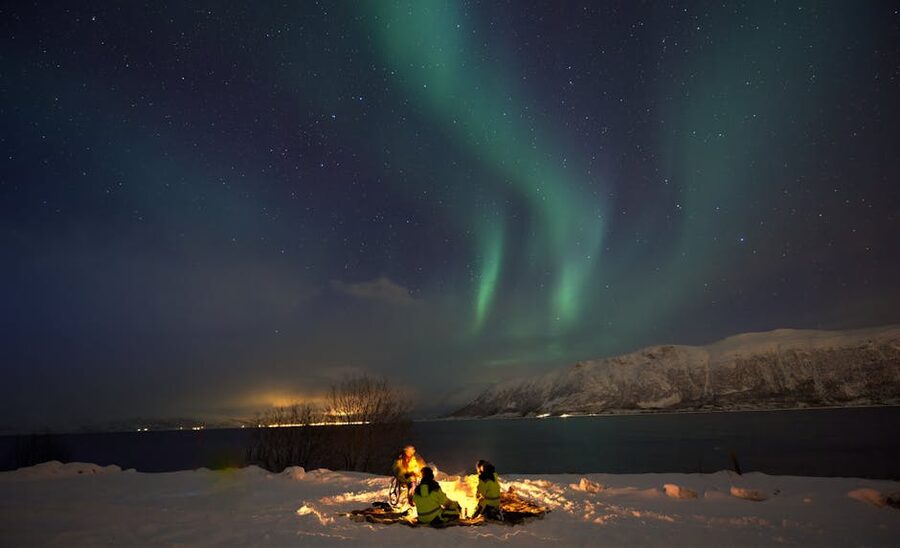 Two people watching the aurora by a campfire near Tromso
